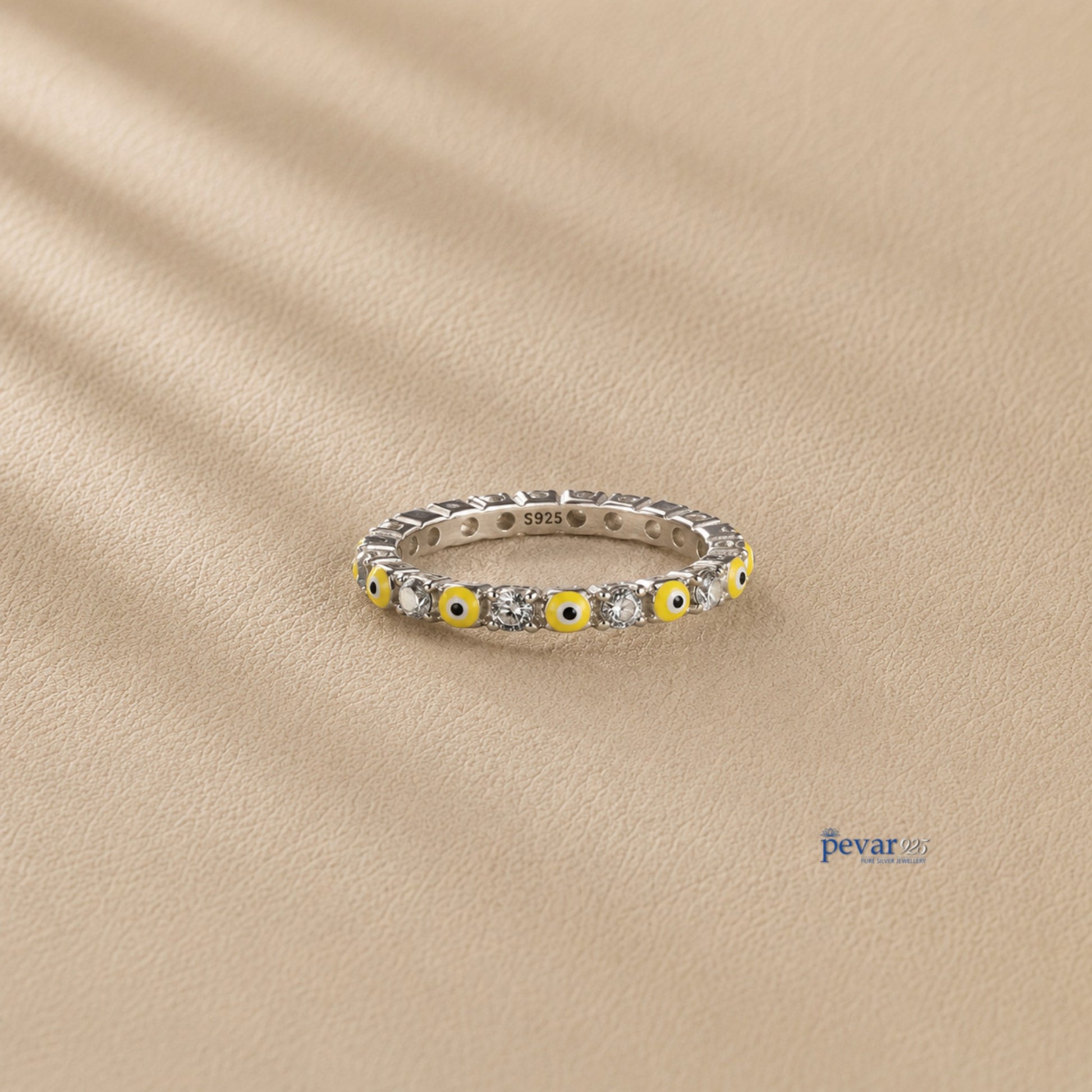 pevar925 sterling silver band ring featuring alternating yellow evil eye motifs and clear stones on a beige background